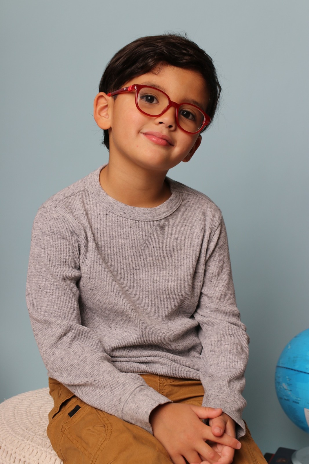 Smiling child in red glasses photographed against a soft blue backdrop